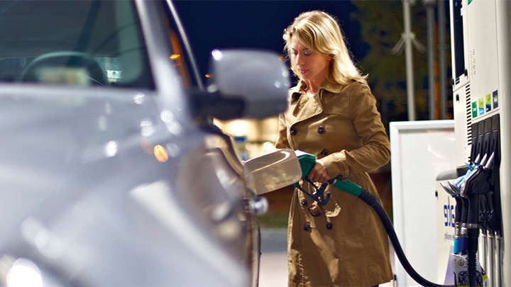 Een vrouw vult bij een tankstation de tank van haar auto onder het heldere licht van Philips luifelverlichting.