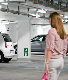 Een vrouw loopt naar een geparkeerde auto in een helder verlichte, duurzaam groene parkeergarage