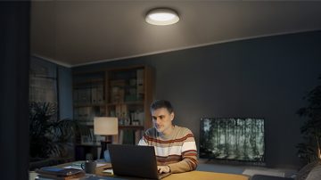 Een man zit aan een bureau met een laptop, van boven verlicht door een ronde plafondverlichting