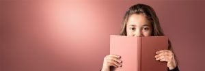 "Jong meisje gluurt over roze boek tegen zachte achtergrond met LED-verlichting, met warme, gelijkmatige verlichting voor comfortabele leesomgevingen."